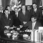 President John F. Kennedy signs the Peace Corps bill in the Oval Office of the White House