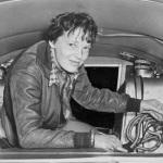 Photo of Amelia Earhart seated in airplane, checking equipment 